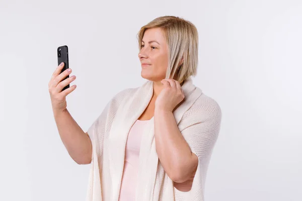 Senior blond kvinna ler och videosamtal via smartphone. Skönhetsbloggning online. Ungdomselixir motivation. Vit bakgrund. — Stockfoto