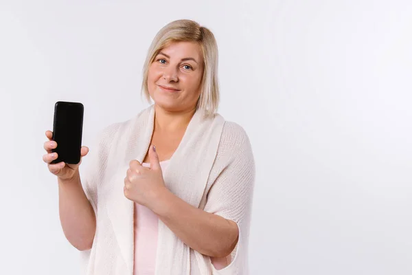 Mujer mayor sosteniendo el teléfono inteligente en las manos mostrando la clase en la cámara. Fondo blanco y espacio lateral vacío. —  Fotos de Stock