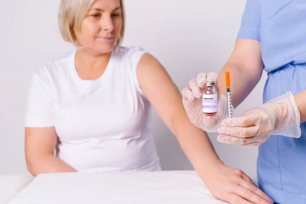 Mujer mayor y manos de una enfermera que sostiene una jeringa y una vacuna para el covidio 19. Lucha contra la propagación del virus en un fondo blanco. — Foto de Stock