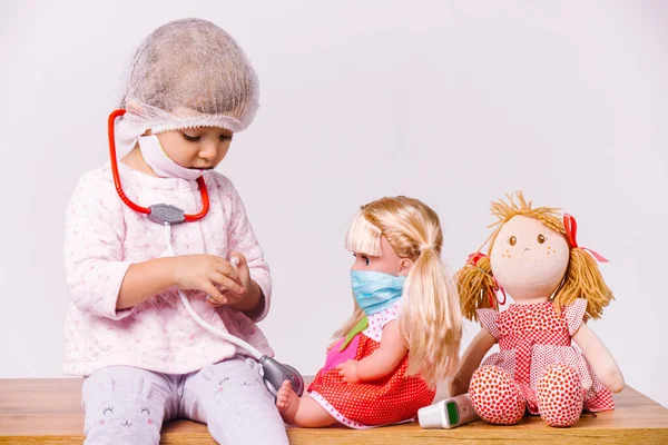 Una niña preescolar interpreta a un médico infantil y trata a las muñecas sobre un fondo blanco. — Foto de Stock