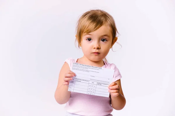 Niña con una tarjeta de vacunación mira a la cámara sobre un fondo blanco con espacio lateral en blanco. — Foto de Stock