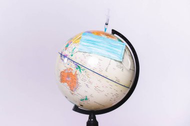 Büyük küre, tıbbi maske ve aşı şırıngası. Beyaz arkaplan ve yan alan üzerine küresel koronavirüs salgını kavramı.