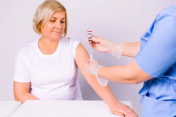 Mujer rubia mayor esperando la vacuna contra el coronavirus. Manos de enfermera preparan jeringa y ampolla de vacuna covid 19. — Foto de Stock