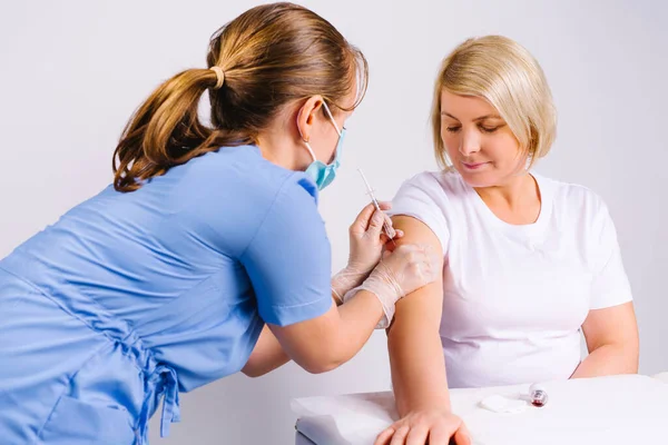 Un médico de uniforme médico azul le pone la vacuna con una jeringa a una mujer rubia mayor. Fondo blanco. — Foto de Stock