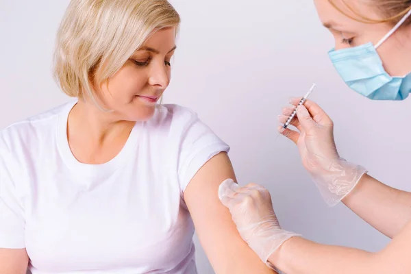 Beskuren bild. En sjuksköterska gav en äldre kvinna ett vaccin mot covid 19. Vit bakgrund. Bekämpa spridningen av viruset. — Stockfoto