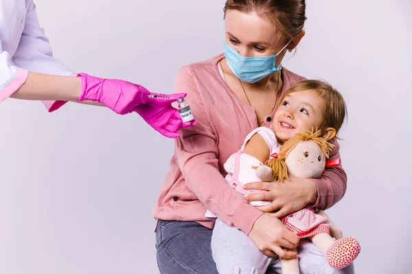 Mamá y la niña son felices en una clínica infantil reciben una vacuna contra el covidio 19. Fondo blanco y enfoque para los niños pequeños. — Foto de Stock