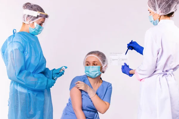 Una enfermera prepara una jeringa con una vacuna para una joven doctora. Y le dan un certificado de vacunación en un fondo blanco. — Foto de Stock