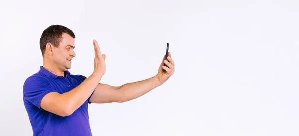 Banner,long format. A deaf man with a hearing aid waves his hand in front of the camera while communicating through social networks via a smartphone. White background and empty side space. — Stock Photo, Image