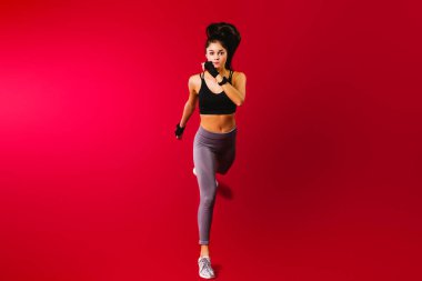 Sportif kız koşar ve kameraya bakar. Kırmızı arkaplanda çalışan ve boş yan boşluk. Yan sporu ve sağlıklı reklamı olan uzun bir fotoğraf. Kadın zayıf motivasyonu