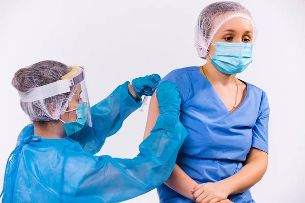 En sjuksköterska i skyddsutrustning placerar ett coronavirusvaccin till en läkare med vit bakgrund. Prioritering av att skydda medicinsk personal under en pandemi. — Stockfoto