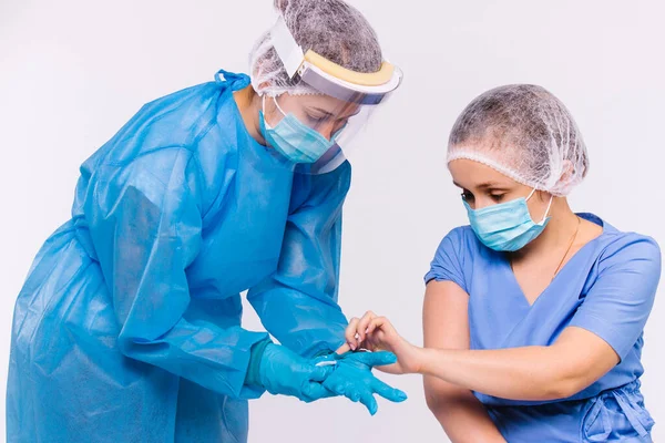 Foto av sjukvårdspersonalen. En sjuksköterska hjälper en läkare i skyddande medicinsk utrustning sätta på latexhandskar på en vit bakgrund. Begreppet bekämpning av spridning av viruset och vaccinering — Stockfoto