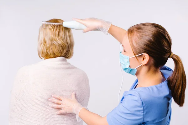 Ung mästare gör darsonvalidering för hår av en blond kvinna på en vit bakgrund. Bakom vyn — Stockfoto