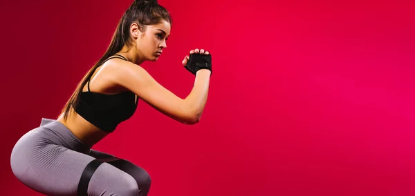 Banner, uzun format. Şişirilmiş bir fitness esmer kız kalçasını ve bacak kaslarını elastik bir bantla sallıyor. Kırmızı arkaplan.