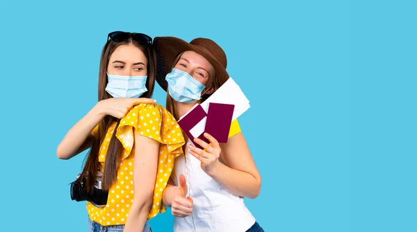 Conceito de turismo covid-19 e pandemia. Dois jovens turistas usando máscaras médicas descartáveis, mostrando passaportes, bilhetes de avião, certificado internacional de vacina- ICV, em fundo azul — Fotografia de Stock