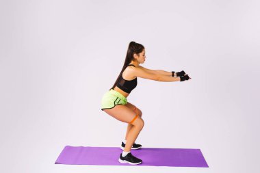 Bir direniş grubuyla çömelmiş genç bir atletik kızın tam boy fotoğrafı. Şişirilmiş kalçalar. Reklam için beyaz arkaplan yan alanı.