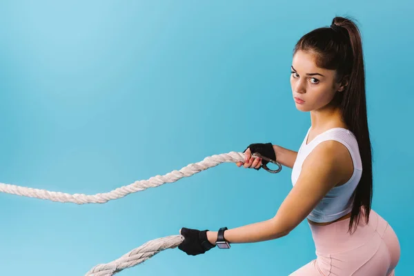 Een foto van de zijkant van een brunette meisje met gespierde bessen die het touw voor haar laat vallen en naar de camera kijkt op een blauwe achtergrond met lege ruimte. — Stockfoto