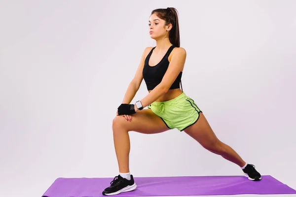 Giovane ragazza bruna concentrata che fa esercizi per allungare le gambe su uno sfondo bianco. Il concetto di sport e un bel corpo gonfiato. — Foto Stock
