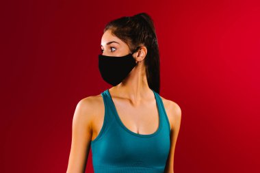 Kırmızı arka planda siyah koruyucu maske takan, reklam alanı olan bir kızın profil fotoğrafı. Salgın sırasında spor konsepti.