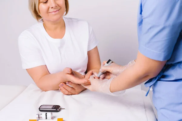 Händerna hos sjukvårdspersonal som använder en glukometer för att ta en analys från en äldre kvinna med vit bakgrund. — Stockfoto