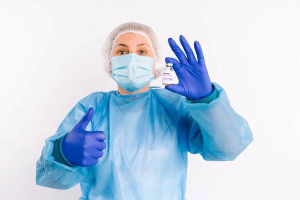 Un paramédico en guardia de protección mira a la cámara que muestra la clase y sostiene una vacuna del covidio 19 en sus manos. Fondo blanco. Pulgares arriba. — Foto de Stock