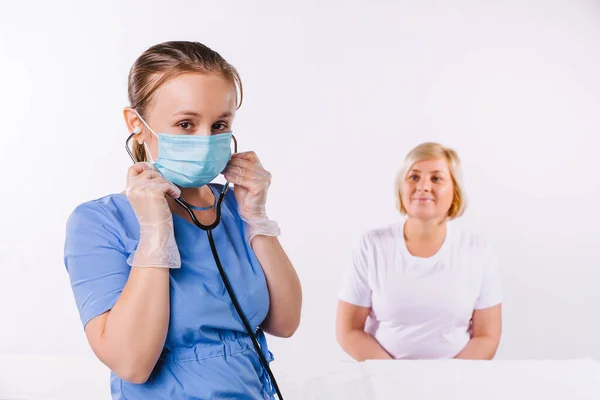 Joven doctora en uniforme y una máscara médica sobre un fondo blanco con una mujer mayor. — Foto de Stock