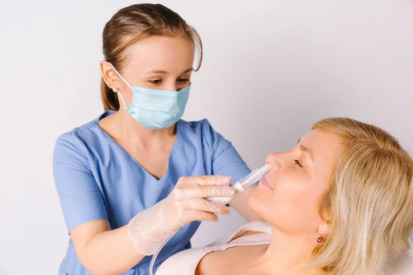 Een jonge arts met een medisch masker inhaleert een oudere vrouw met een witte achtergrond. Neusverstopping en rhinitis bestrijden. — Stockfoto