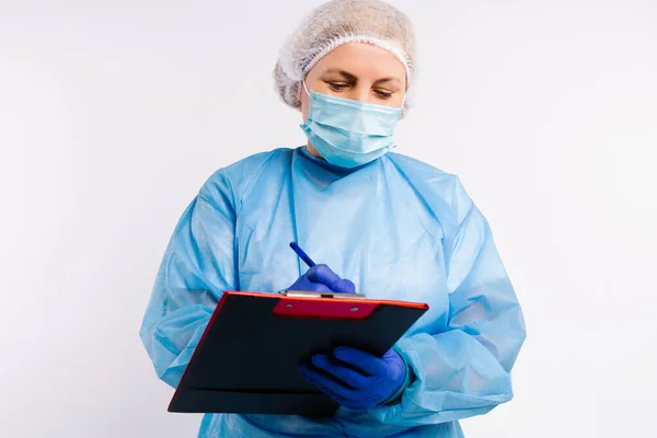 Un medico in attrezzature mediche protettive contro l'infezione Covid 19 che compila elenchi di pazienti su uno sfondo bianco. — Foto Stock