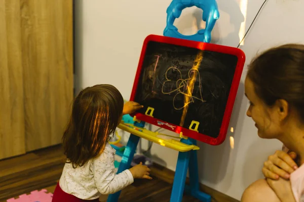 Loisirs familiaux à domicile en cas de pandémie. Maman et petite fille dessinent avec de la craie sur le tableau noir. — Photo