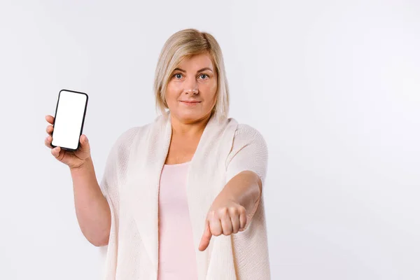 Старшая белая женщина со смартфоном показывает, что палец опущен. Ненависть на белом фоне с боковым пространством. — стоковое фото
