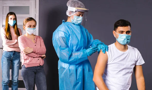 Ofisteki personelin toplu aşısı. Koruyucu giysili bir hemşire bir erkeğin koluna iğne batırır..