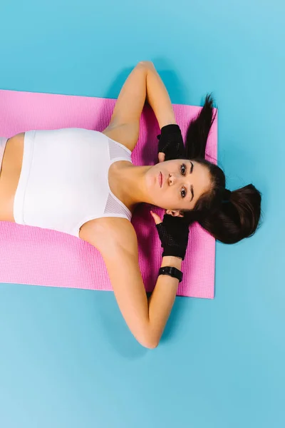 Fitness lány pihenni és pihenni edzés után feküdt egy rózsaszín jóga szőnyegen. Fénykép fentről. Kék háttér. — Stock Fotó