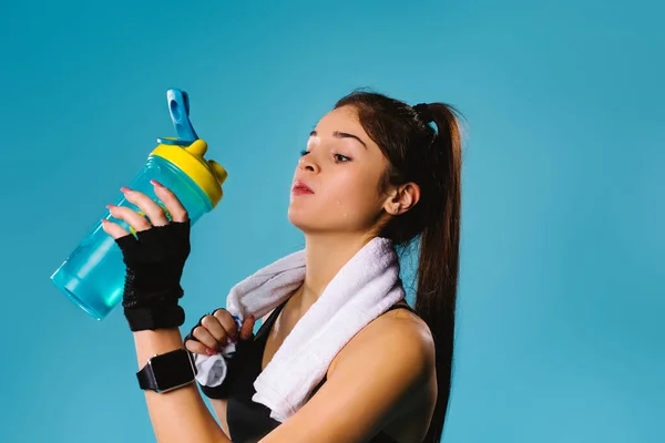 Une belle sportive, après l'exercice, boit une boisson protéinée sur fond bleu avec une serviette sur le cou. Espace latéral. Sports et muscles. — Photo