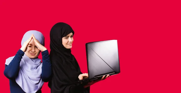 Banner - langes Format. Kaukasische muslimische Frauen sind Maklerinnen. Sie unterzeichnen Online-Deals. Sie verkauften neue Wohnungen. Araberin hält Hände in Form eines Hauses, eine andere hält einen Laptop und blickt auf den Bildschirm. — Stockfoto