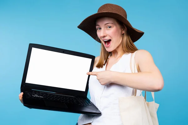 Donna sorpresa in abiti estivi indicando dito indice sul computer portatile PC con schermo vuoto bianco isolato su sfondo blu. Emozioni, viaggi, stile di vita. Spazio di copia Mockup — Foto Stock