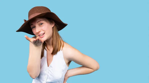 Banner- formato longo. Retrato de uma linda jovem mulher loira caucasiana em chapéu de verão e top branco enviando beijo isolado sobre fundo azul com espaço lateral vazio — Fotografia de Stock