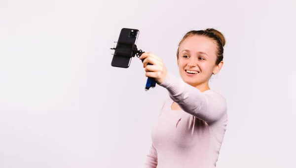 Banner. Blogger menina sorrindo em transmissão ao vivo para assinantes. Um jovem blogueiro segura um smartphone em suas mãos. Fundo branco e espaço lateral. — Fotografia de Stock