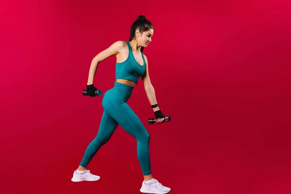 Egy teljes hosszúságú fénykép egy lányról sportruházatban egy fitnesz edzésen súlyzókkal piros háttér mellett oldalsó hirdetési hellyel. — Stock Fotó