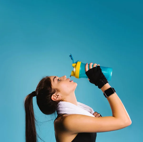 Жінка-спортсменка з рушником на шиї після тренування з спрагою напоїв на синьому фоні. Порожній верхній простір для реклами . — стокове фото