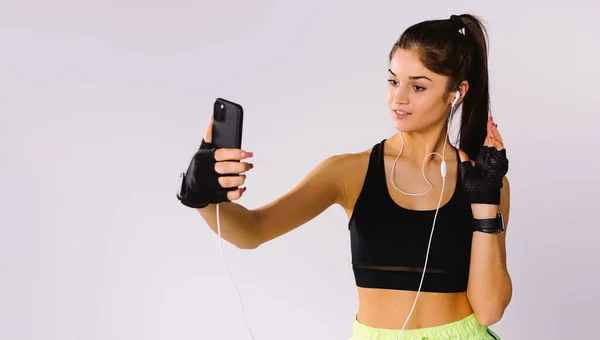 Banner. Caucásico chica en ropa deportiva hace un selfie en un teléfono inteligente sonriendo sobre un fondo gris. —  Fotos de Stock