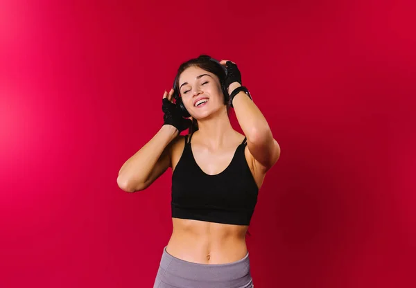 Een vrolijk meisje met een mooie lichaamsbouw met een glimlach luistert naar muziek in grote koptelefoons op een rode achtergrond met lege zijruimte. — Stockfoto