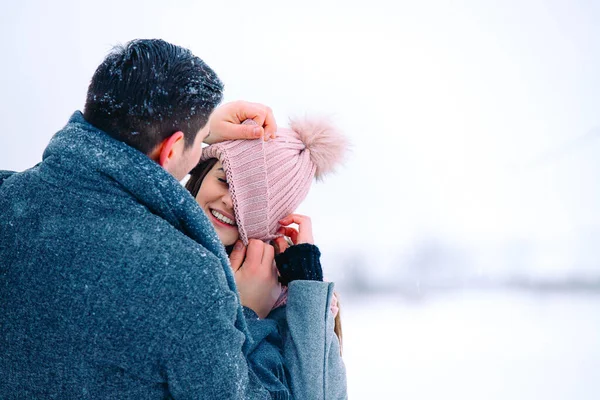 Photo arrière de l'homme aimant tirant vers le bas sa petite amie riante chapeau rose, s'amuser ensemble à l'extérieur, profiter de la journée d'hiver, temps neigeux. Couple mignon jouant dans le parc. Espace vide latéral — Photo