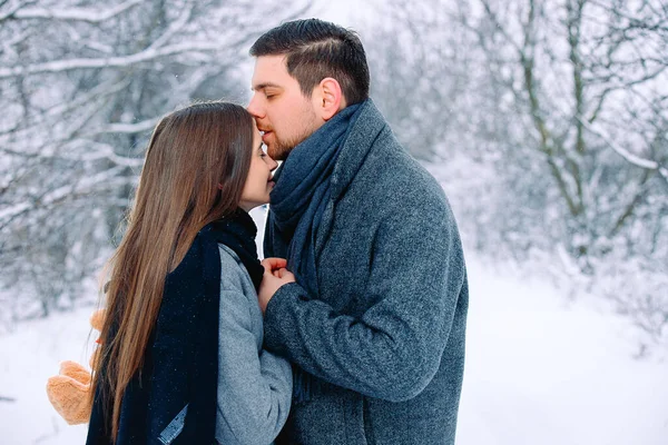 Καυκάσιο ζευγάρι στο χειμερινό πάρκο. Νεαρή μελαχρινή αξιαγάπητη άντρας φιλάει γυναίκες στο μέτωπο. Πλευρικό λευκό κενό — Φωτογραφία Αρχείου