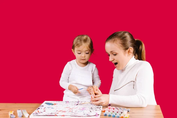 Les devoirs pendant la pandémie. Jeune famille. Maman et fille bordent le tableau par des chiffres aux couleurs vives. Fond rouge et espace publicitaire latéral. — Photo