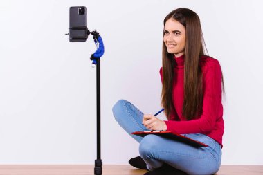 Beyaz kız öğrenci internet kurslarını akıllı telefondan dinliyor ve bilgi kaydediyor. Boşluğu olan beyaz arkaplan.