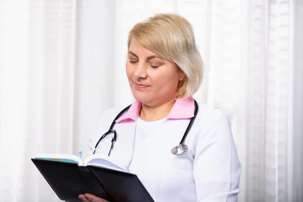 医学杂志上的专业医生笔记 穿着白衣的女医生或药剂师 记事本 重点关注老年医生在医务室书写病史 高质量的照片 — 图库照片
