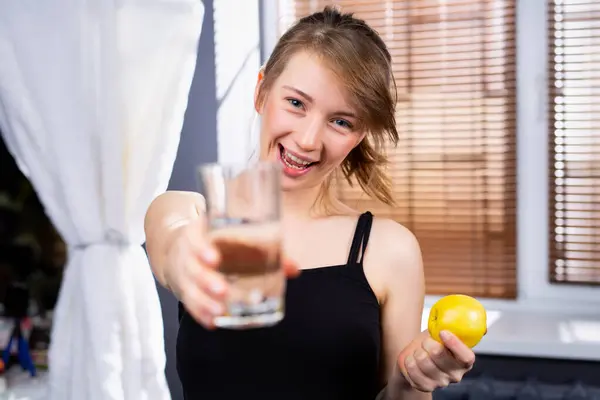 Молода Жінка Посміхається Тримаючи Склянку Води Перед Камерою Внутрішній Фон — стокове фото