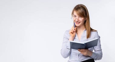 Sancak- uzun format. Resmi olarak güzel bayan öğretmen not defterine yazıp sınıfta kameraya bakıyor. Gri arkaplan ve geniş alan. Yüksek kalite fotoğraf