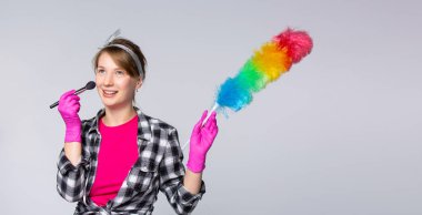 The concept of house cleaning. Surprised young woman from the cleaning service, she is wearing a colorful dust brush and a makeup brush, dressed in a casual T-shirt. High quality photo