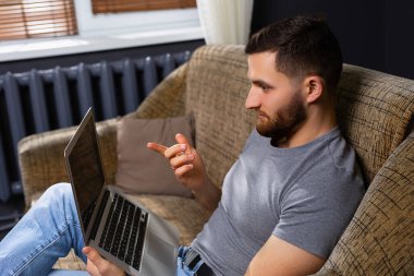 Dizüstü bilgisayarı olan bir adamın profil fotoğrafı. Salgın sırasında iş arkadaşlarıyla video konferansı. Rahat bir kanepede otururken evden çalışmak. Yüksek kalite fotoğraf