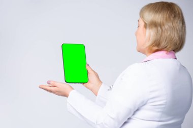 Kafkas kadın doktor yeşil tablet ekranla hastanedeki hastaya muayene yapıyor. Doktor cihaza işaret ediyor ve gösteriyor, boş ekran tableti. Sağlık ve Tıp Konsepti.